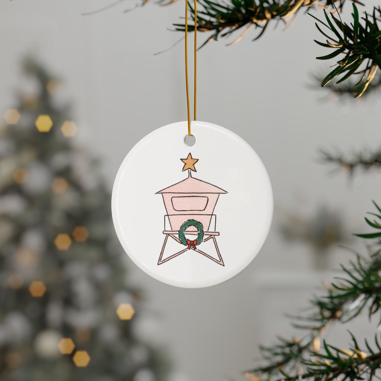 Round Christmas ornament with a lifeguard stand design featuring a wreath and a star, hanging on a Christmas tree.