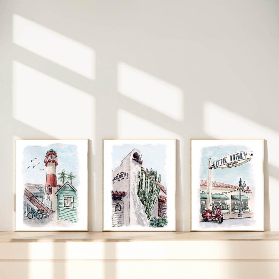 Set of three hand-painted watercolor artworks featuring coastal lighthouse with a red-and-white tower, Old Town San Diego adobe building with cacti, and Little Italy San Diego street sign with a classic red Vespa. Framed in light wood, perfect for travel-inspired home decor by Swil Arts.