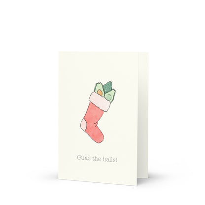 Greeting card with a Christmas stocking filled with avocados illustration and text that reads: "Guac the halls" on a white background