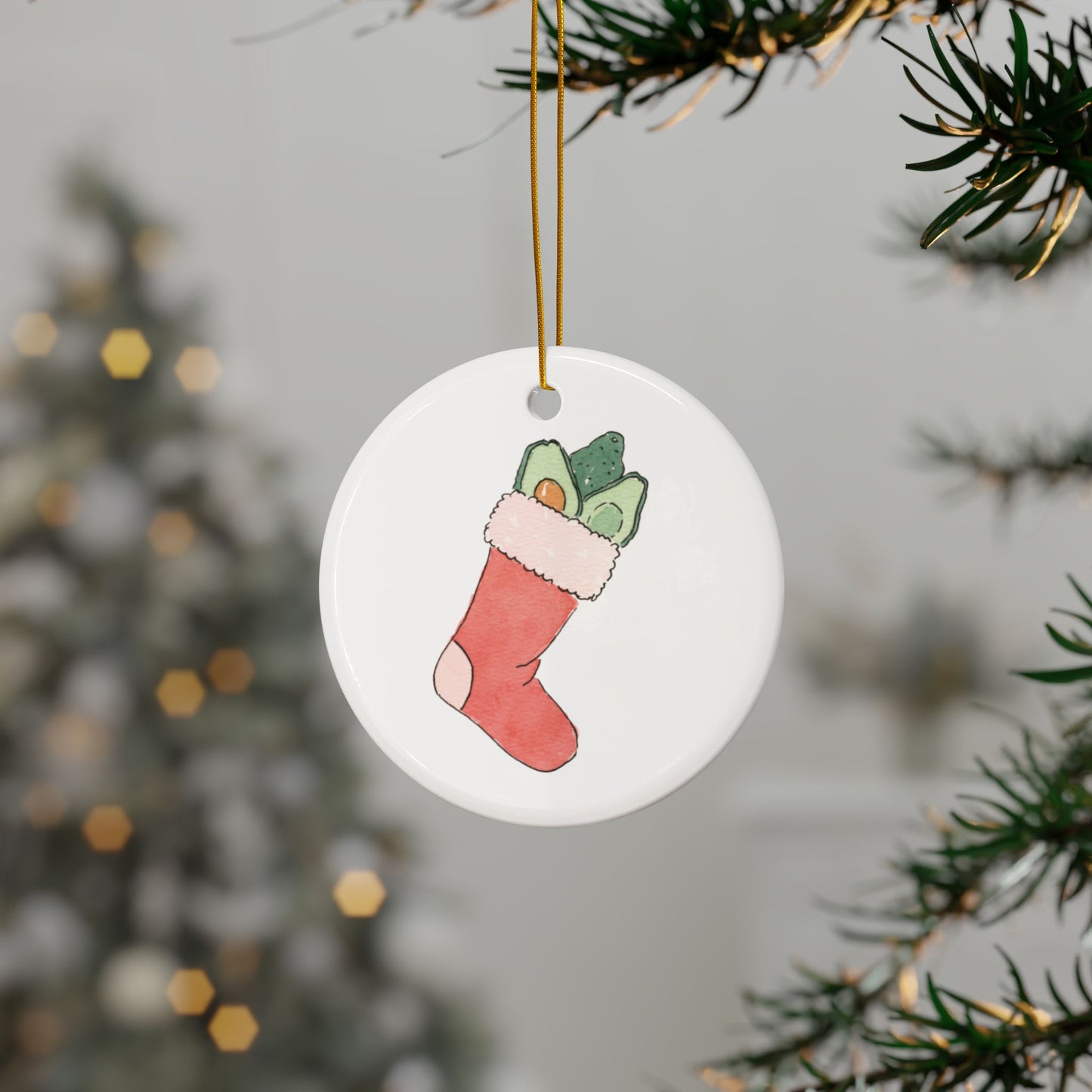 Round ceramic ornament with a Christmas stocking filled with avocados design hanging on a tree branch.