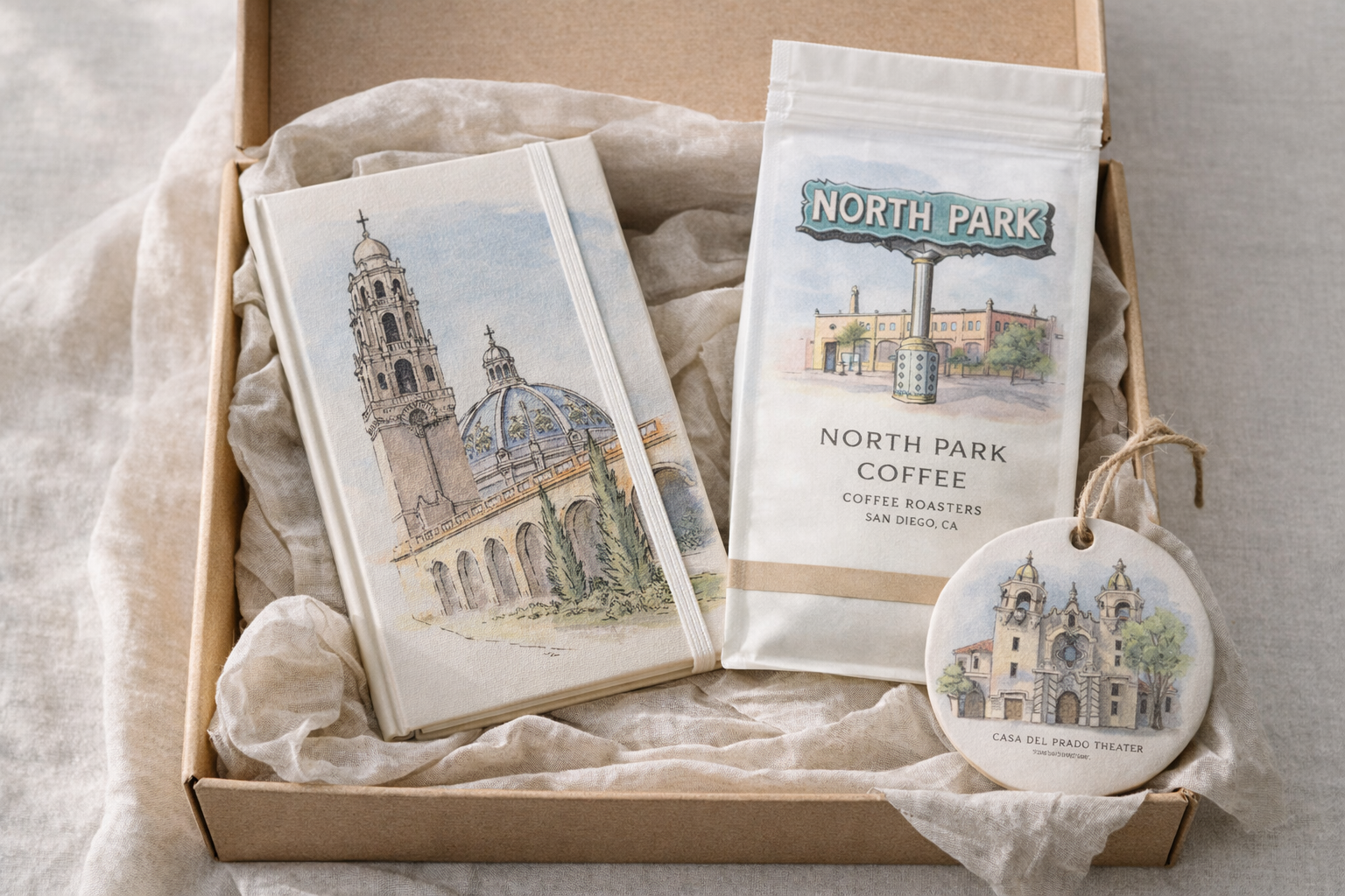 Gift set with coffee package, postcard, and ornament all illustrated by Sara from Swil Arts. The notebook has the California Tower from Balboa Park. The coffee has the North Park sign. The ornament has Casa del Prado Theater.