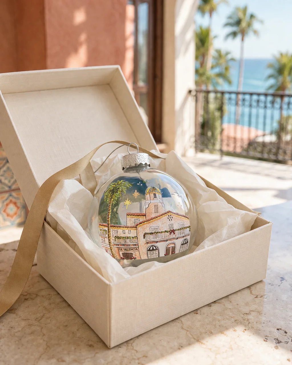 Decorative glass ball with illustration of La Valencia Hotel made by Sara from Swil Arts, in an open box with a scenic background