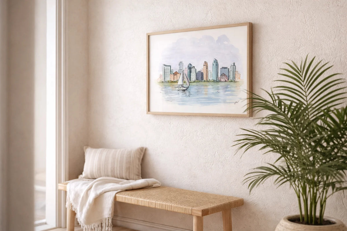 Framed cityscape painting on a wall above a wooden bench with a plant to the right.