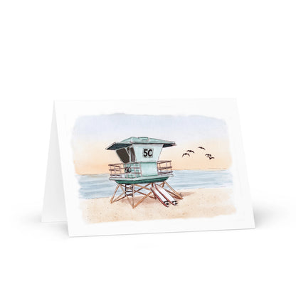 The Southern California Greeting Card Box Set - Watercolor Art showcases a lifeguard tower 5C on a sandy beach with ocean waves and four birds—ideal for fans of coastal stationery and SoCal-inspired cards.
