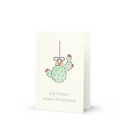 Card with a cactus ornament illustration and text on a white background that reads "Joy blooms where it's sunniest"