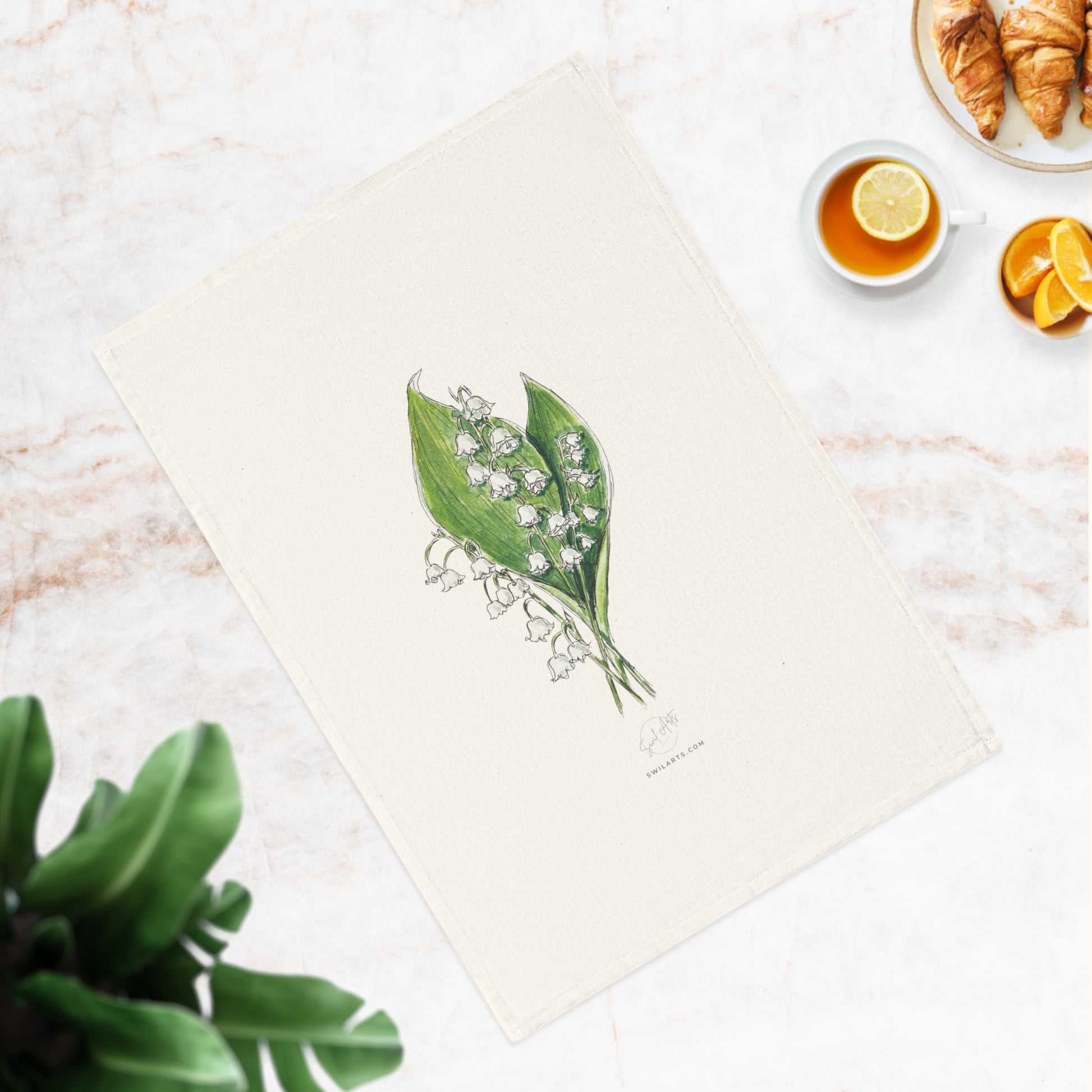 Botanical watercolor tea towel featuring a lily of the valley flower illustration by Swil Arts. This elegant, eco-friendly kitchen towel showcases a delicate ink and watercolor rendering of white lily of the valley with green leaves on a soft, neutral fabric. A perfect blend of art and functionality, this nature-inspired tea towel adds a touch of botanical beauty to any kitchen or dining space. Ideal for floral enthusiasts.