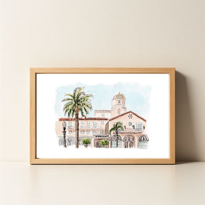 Watercolor painting of a pink building with palm trees in a wooden frame.