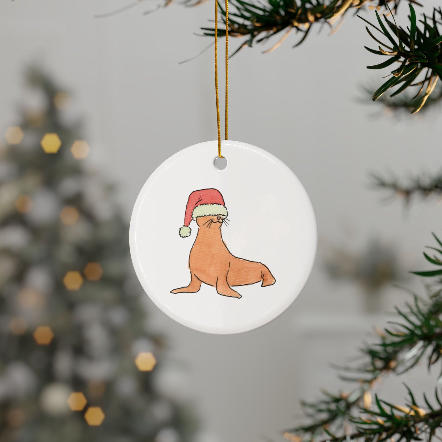 Round ceramic ornament with a seal wearing a Santa hat, hanging from a Christmas tree.