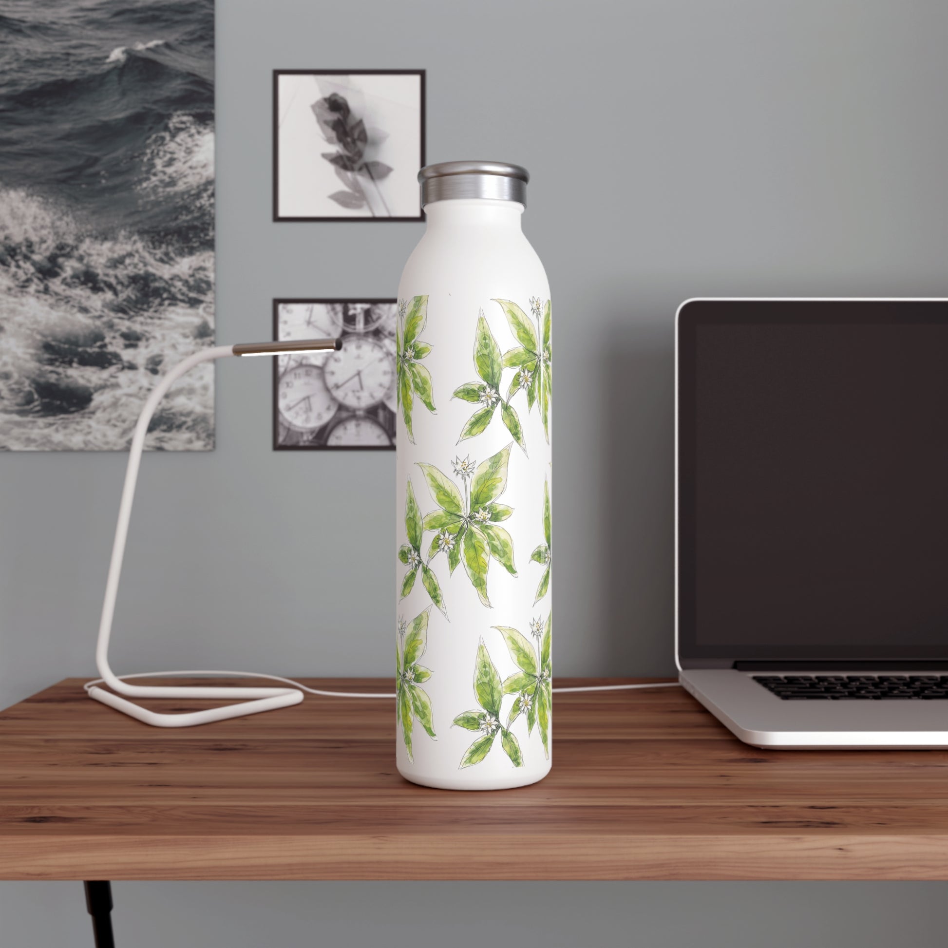 White stainless steel water bottle with a  starflower watercolor design, placed on a wooden desk with a laptop, modern lamp, and black-and-white wall art in the background.