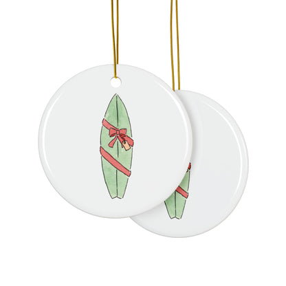 Two round ceramic ornaments with green surfboards and red bows on a white background