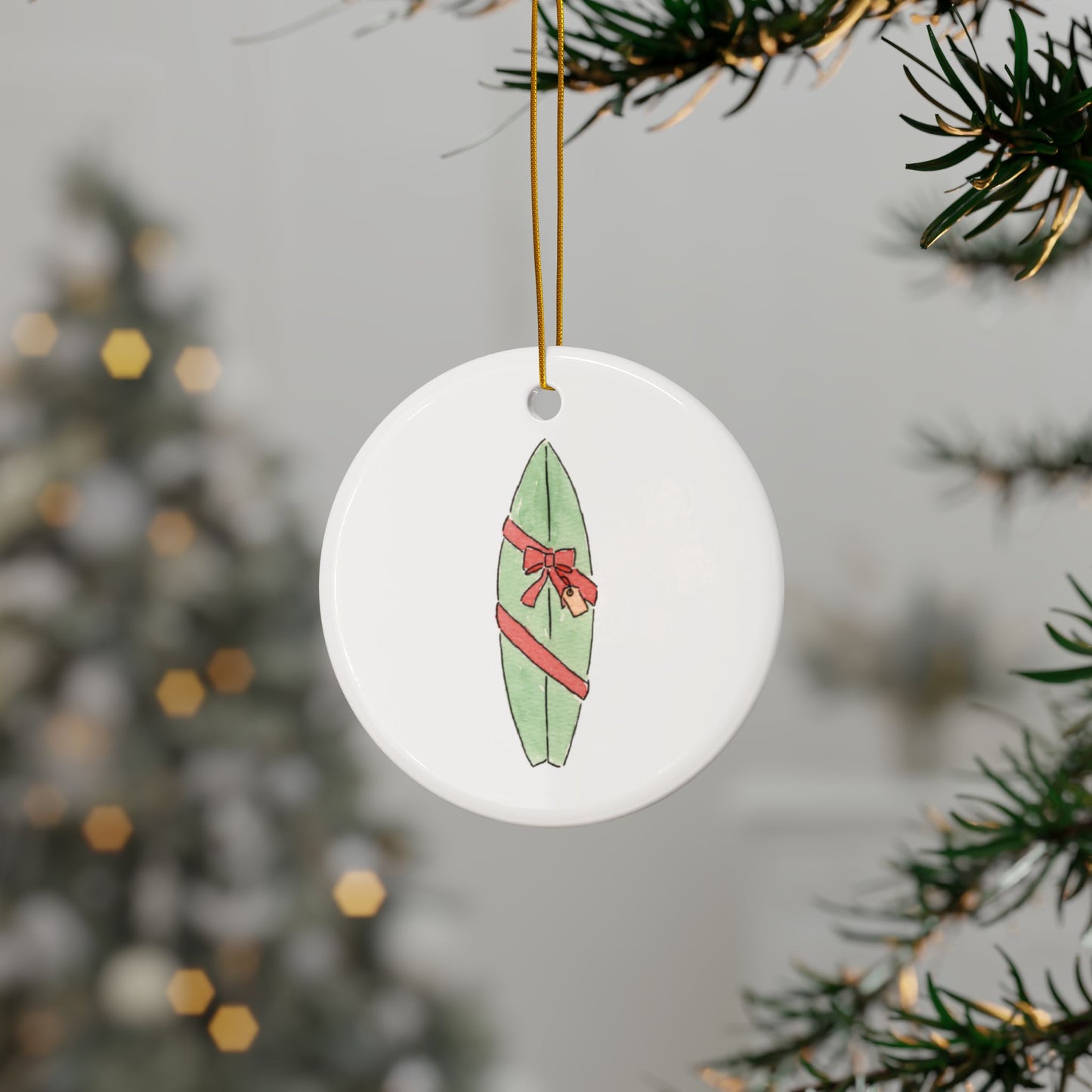 Round Christmas ornament with a green surfboard wrapped as a gift design hanging on a Christmas tree branch.