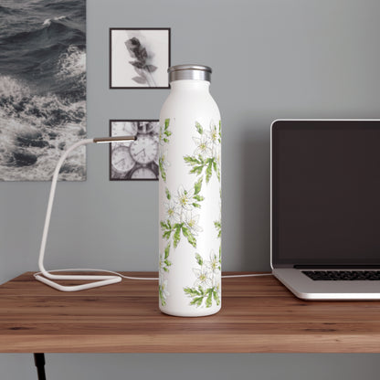 White stainless steel water bottle with a wood anemone flower watercolor design, placed on a wooden desk with a laptop, modern lamp, and black-and-white wall art in the background