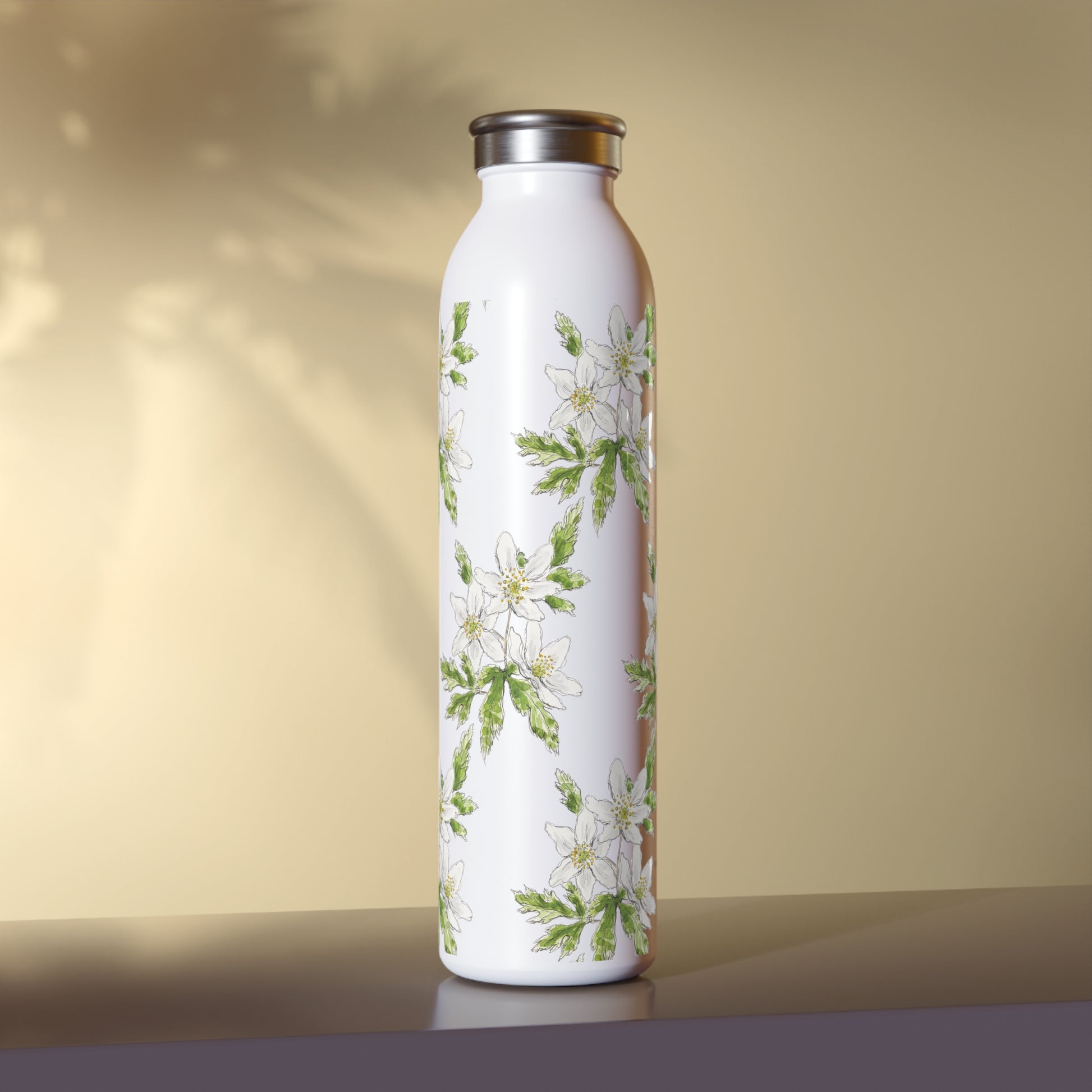 White stainless steel water bottle featuring a wood anemone flower watercolor pattern, set against a warm beige background with soft leaf shadows.