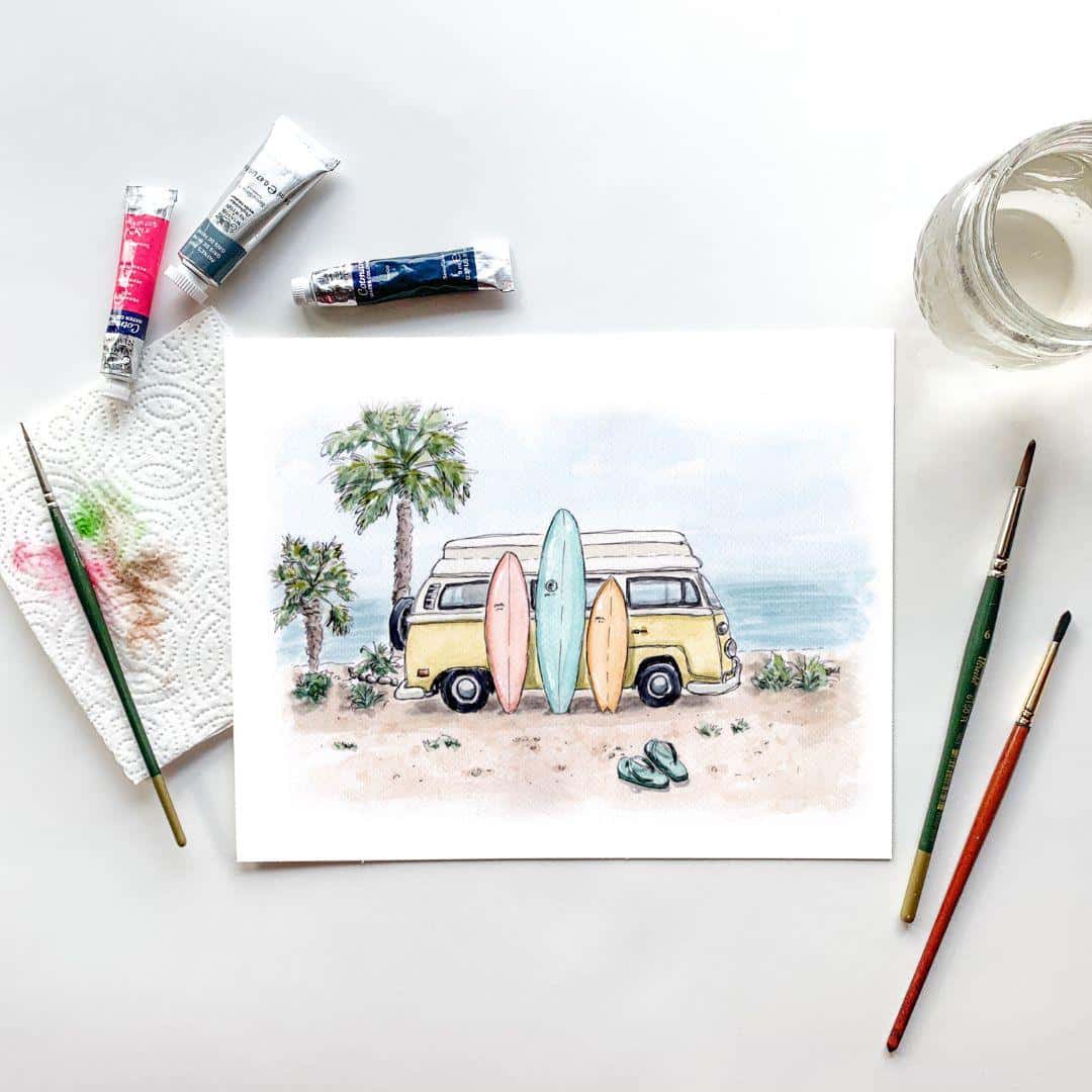 Watercolor painting setup featuring a beach scene artwork of a yellow camper van with surfboards, surrounded by art supplies. The scene shows a jar of water, paintbrushes, watercolor tubes, and a paper towel with paint, evoking the creative process behind the coastal-themed painting.