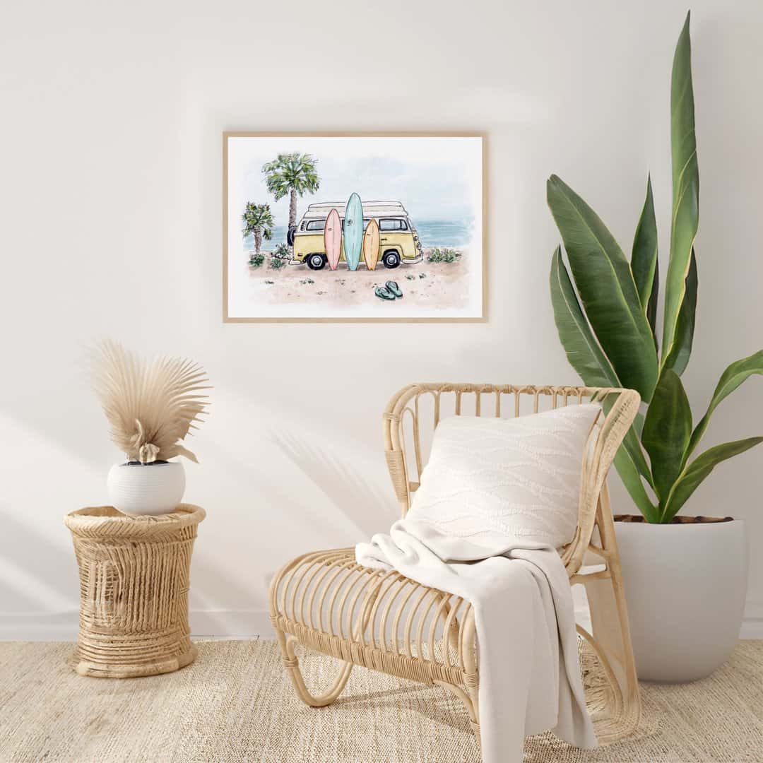 Framed watercolor print of a beach scene with a yellow camper van and surfboards, displayed in a modern, coastal-style living room with rattan furniture and neutral tones. The artwork adds a laid-back, beachy vibe to the minimalist, nature-inspired decor.