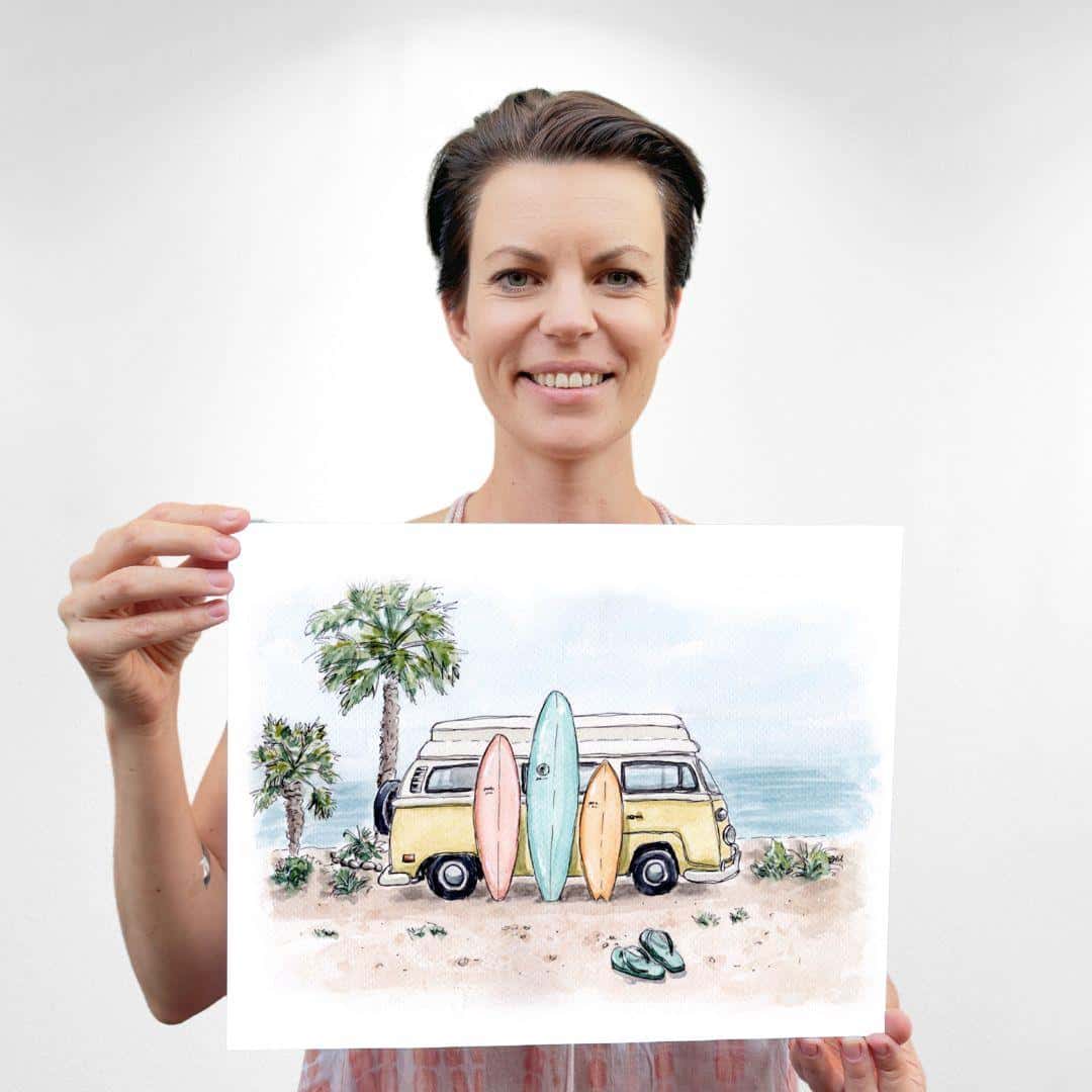 Sara, the artist behind Swil Arts is smiling and holding a watercolor print of a beach scene featuring a yellow camper van parked by palm trees, with three colorful surfboards leaning against it. The art captures a serene coastal, Southern California setting with soft pastel tones, perfect for beach and surf lovers.