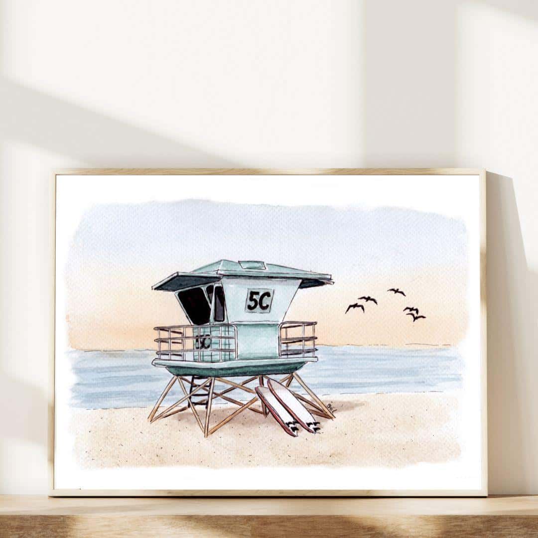 Watercolor print of a lifeguard tower labeled '5C' on a serene beach at sunset, with birds flying in the sky and calm ocean waves in the background. Coastal wall art in a wooden frame, perfect for beach lovers and seaside decor