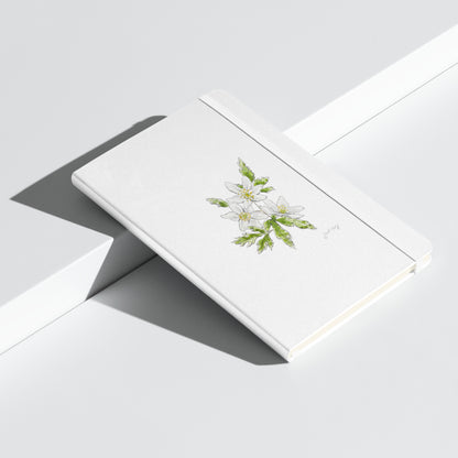 White hardcover notebook featuring a delicate wood anemone flower illustration by Swil Arts. This botanical watercolor and ink design showcases the beauty of nature, making it perfect for journaling, sketching, or note-taking. The notebook includes an elastic closure for convenience, ideal for artists, writers, and nature lovers seeking elegant stationery with a floral touch.