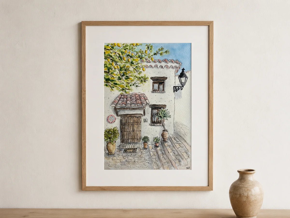 Framed watercolor artwork of a quaint street scene with a building and tree on a beige wall. Arwork by Swil Arts.