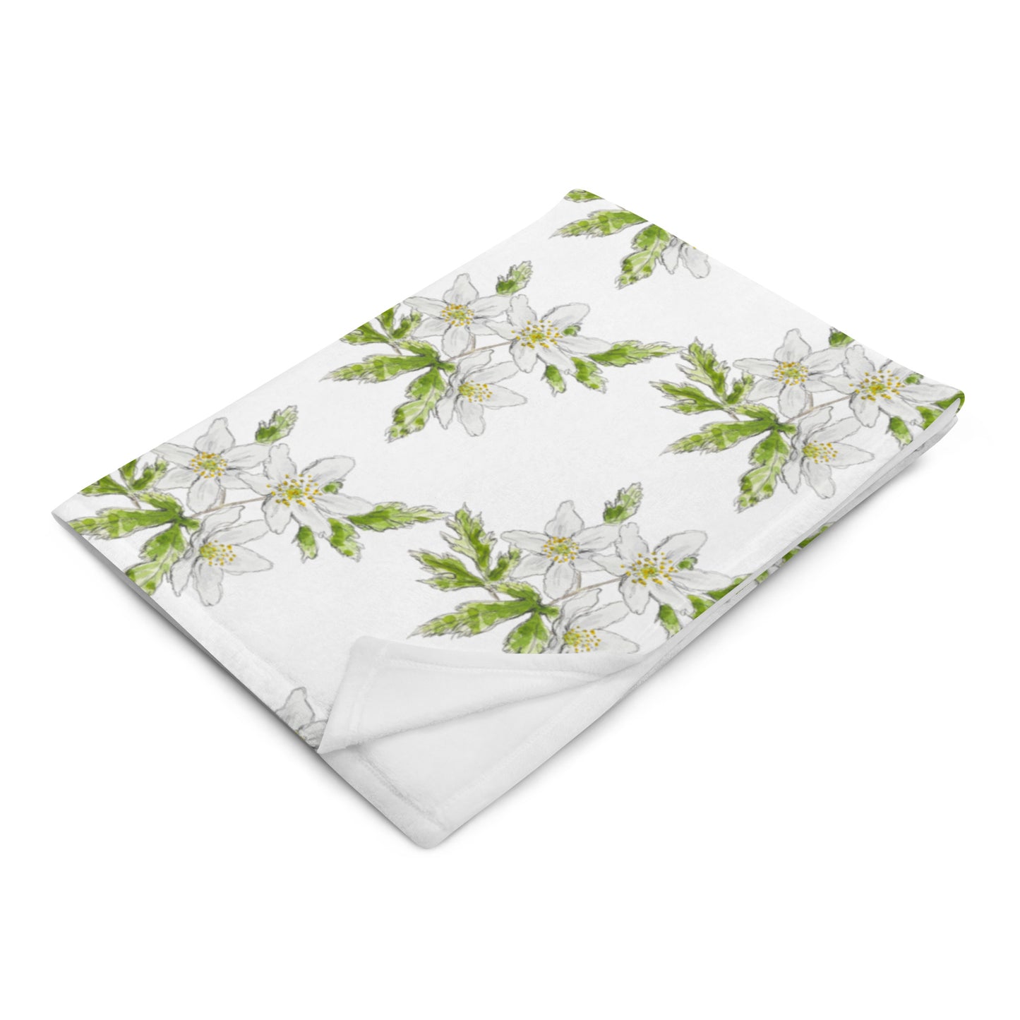 Soft fleece throw blanket featuring a white wood anemone flower pattern with green leaves, elegantly folded on a white surface. Cozy botanical home décor with nature-inspired watercolor design.