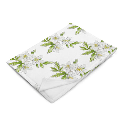 Soft fleece throw blanket featuring a white wood anemone flower pattern with green leaves, elegantly folded on a white surface. Cozy botanical home décor with nature-inspired watercolor design.