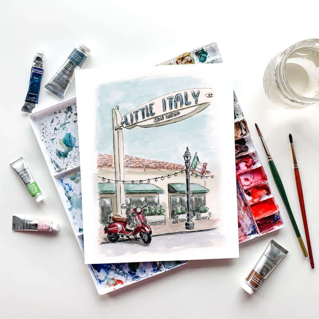 Watercolor painting of Little Italy San Diego with red Vespa scooter, displayed with artist's paint palette and brushes, handmade travel-inspired artwork for modern decor, Italian-themed wall art, perfect for gifts and home decoration
